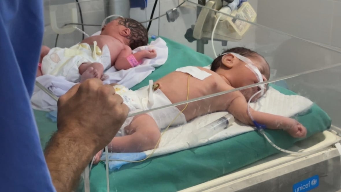 Two babies are in the bed of the hospital as the doctor is watching.
