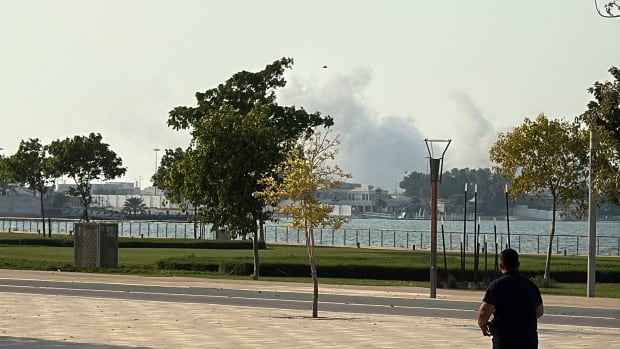 Smoke rises as an onlooker watches from afar.