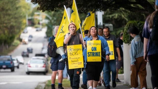 People walk carrying yellow picket signs. 