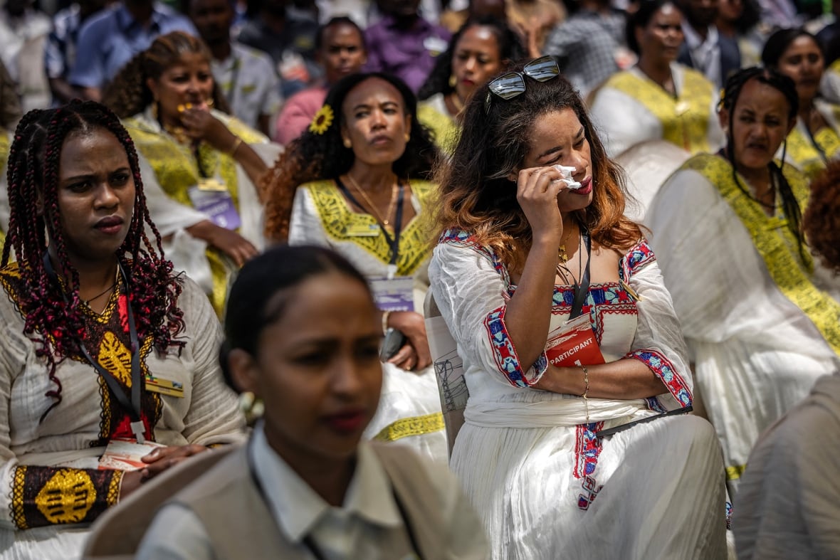 A woman dabs tears from her eyes while seated in a large crowd.