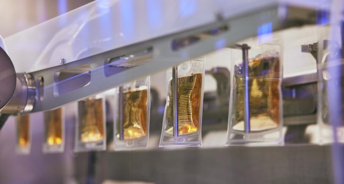 Small plastic bags are filled with a golden colour liquid by a machine. 