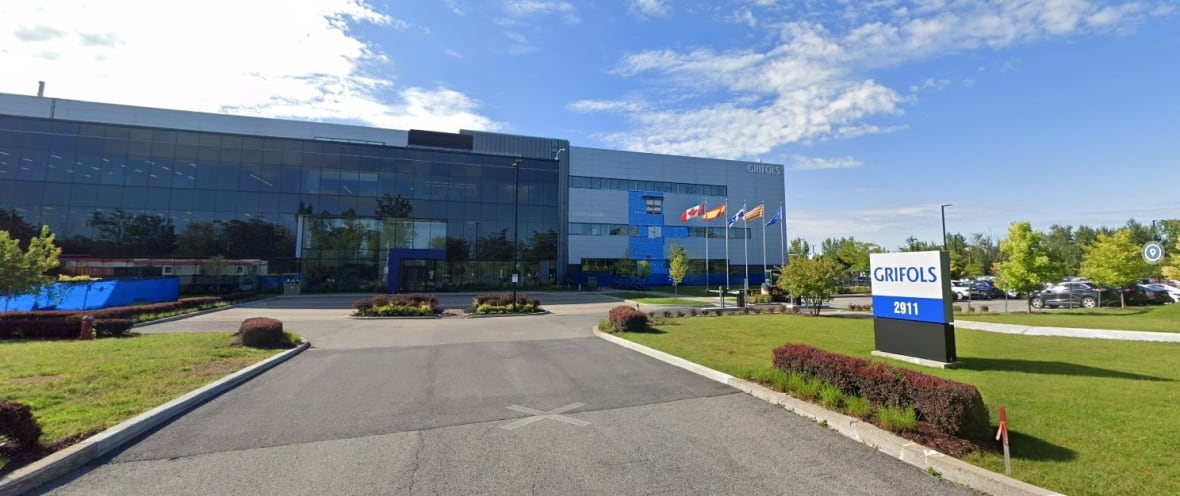 A large building with lots of windows, and a long entrance surrounded by manicured grounds, with a sign out front that says Grifols 2911.