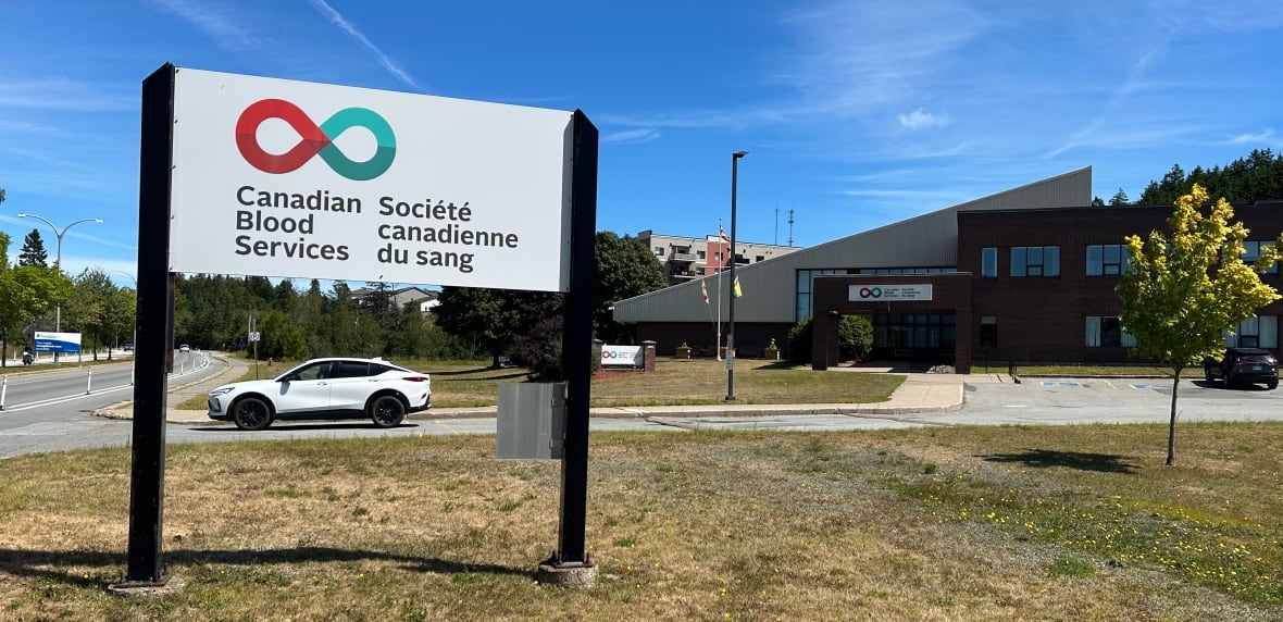 A Canadian Blood Services sign in front of a brick building on a sunny, summer day with burnt grass. 