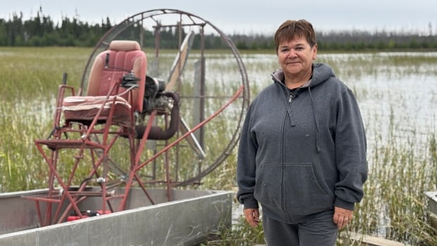 Woman with short hair and sweatshirt stands next to boat with rice plants in background
