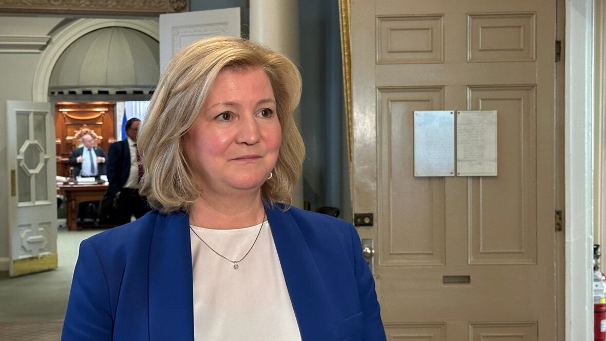 Woman with blond hair wears a blue blazer with a white shirt and a necklace.