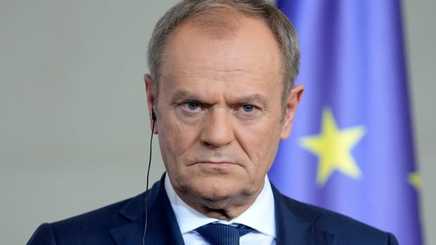 Deputy Defence Minister Cezary Tomczyk said in a post on X that Poland's Prime Minister Donald Tusk, who is pictured listening to the media in Berlin in March 2024, is "present at the scene of the operations." A man scowls in a blue suit in front of a blue European union flag.