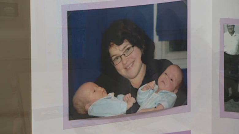 A photo of a woman with dark hair and glasses smiling while holding two infants.