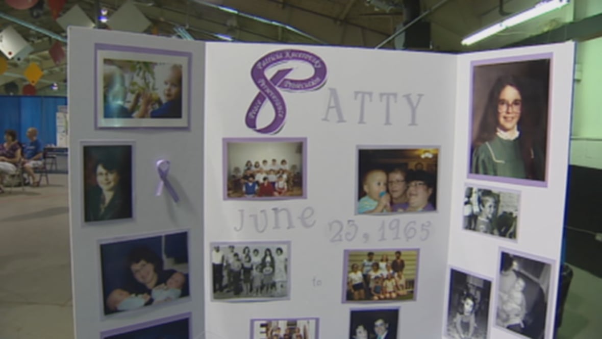 An in memory-style white poster board with the words "Patty, June 23, 1965" on it. There are many photos framed in purple, and a purple ribbon attached.