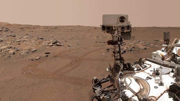 A car-like rover sits on a red, dusty landscape.