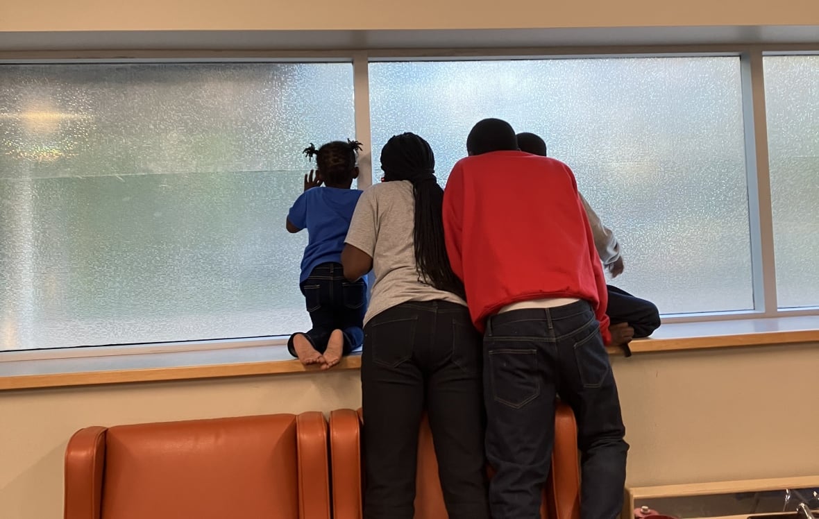 Two children and two adults stand on chairs to peer out a window.