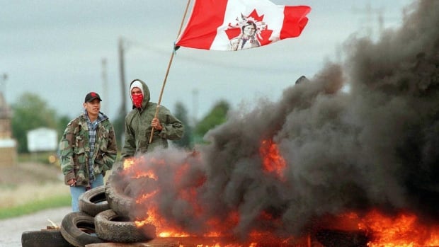 People stand holding a flag behind a burning pile of tires.