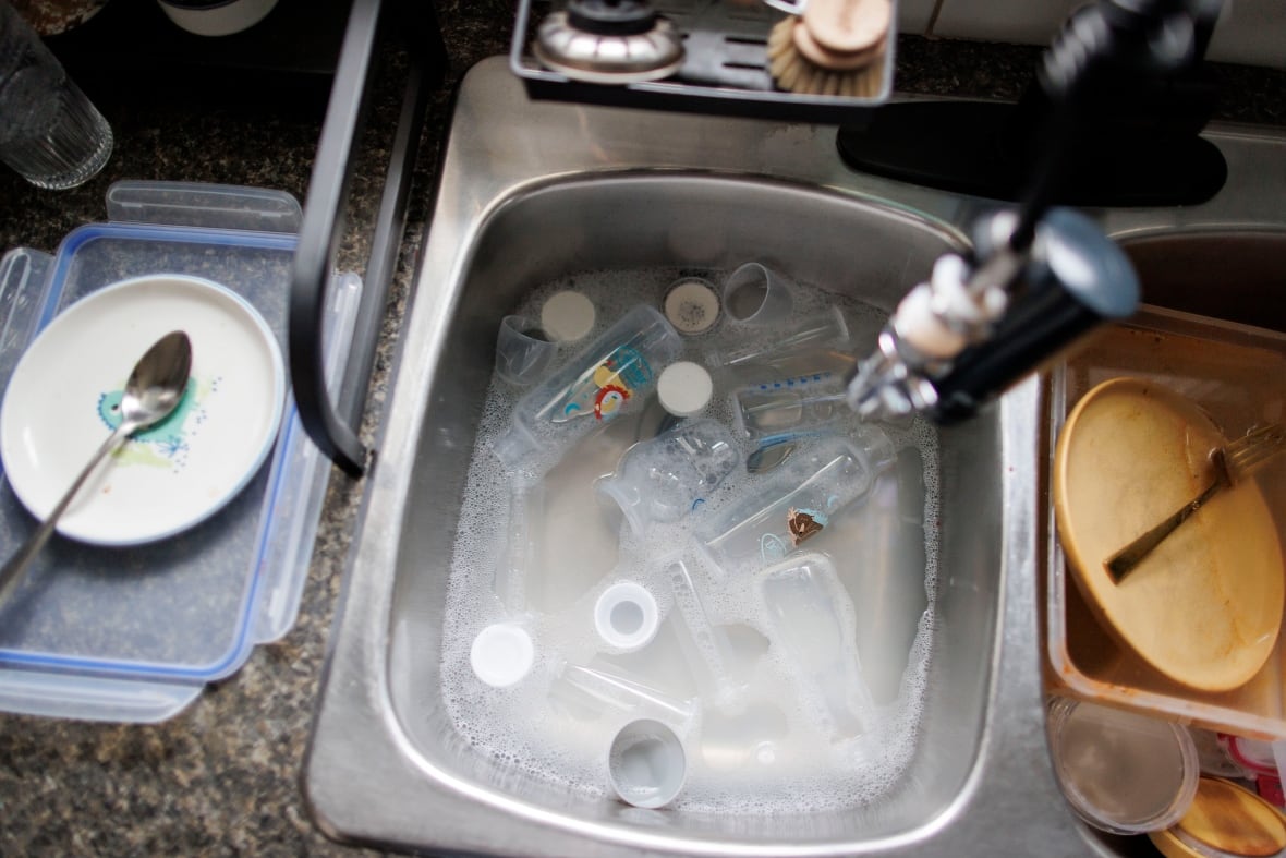 A kitchen sink is full of soaking baby formula bottles.