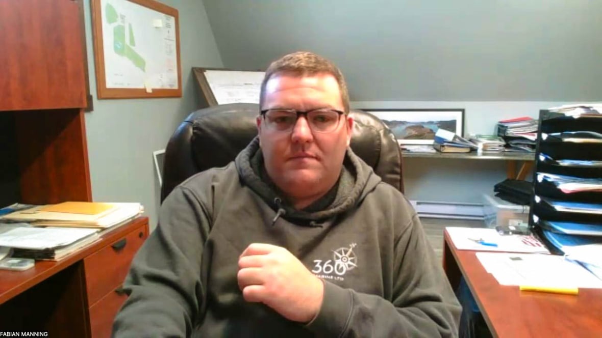 A man with glasses and. brown hair, wearing a green hoodie, looks into the camera