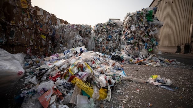 A pile of flexible plastics sit on the ground with tall bales of them behind.