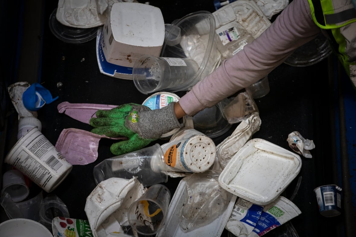 Plastic containers appear on a conveyor belt as a person picks through them.