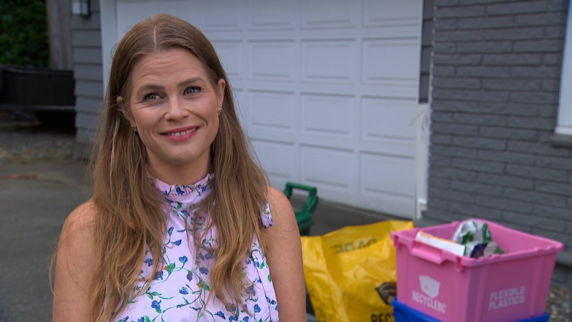 A women with long brown hair smile as she stands by a pink box at her house.