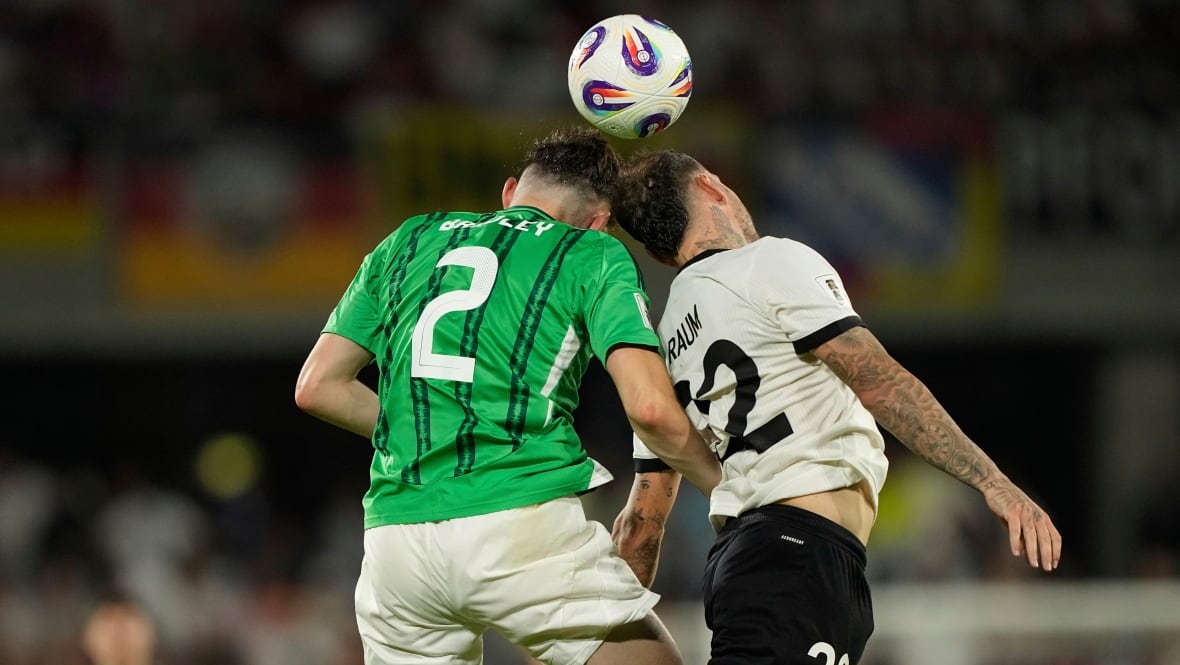 Two soccer players, and their back to the camera, approximately head to the ball.