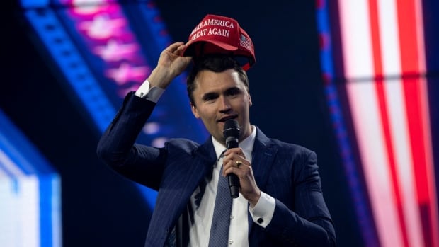 A man putting a 'MAGA' hat on his head.