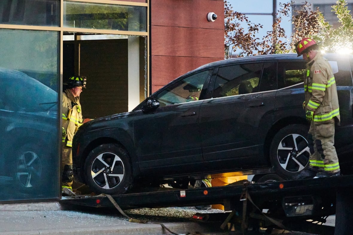 Firefighters stand nearby as a car is pulled out of a window.