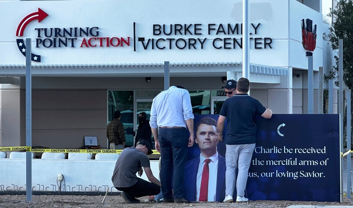 Three men stand before the banner read 'May Charlie find in Jesus' army armies, our loving Savior,' without outside the headquarters of the USA.