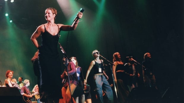 A photograph of Diana Krall, Sarah McLachlan, Angélique Kidjo, Lisa Loeb, Sam Bettens and Tara MacLean on a stage at Lilith Fair in 1998. 