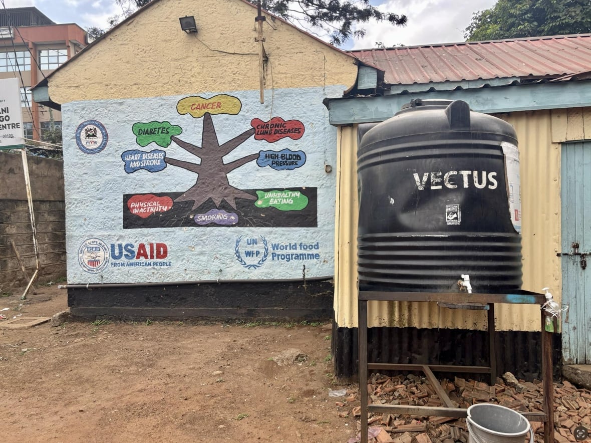 The outer surface of the Swop Majengo clinic. There is a wall with a plate on it and the water tank. 