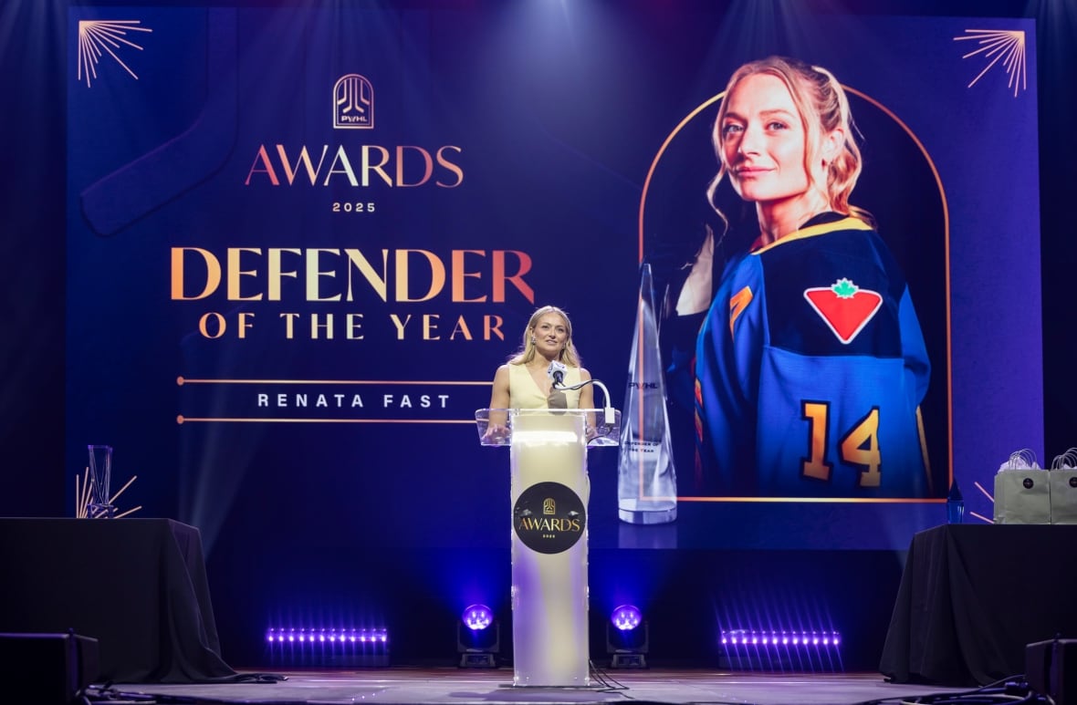 A woman stands at a podium with a big screen behind her.