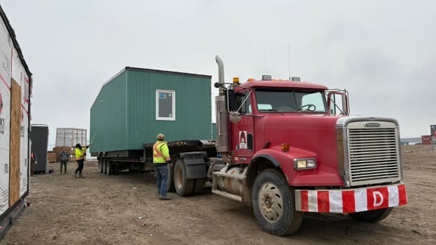 Crews load building onto truck flatbed.
