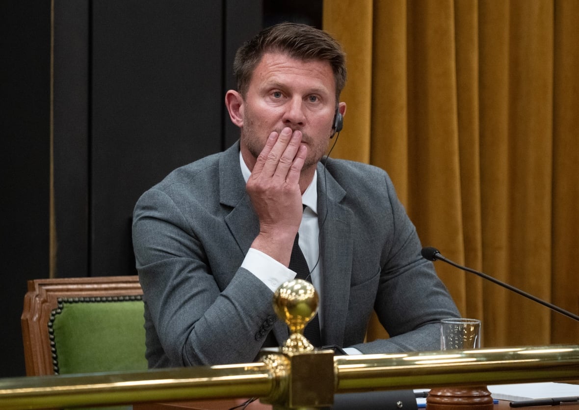 A man rubs his chin as he sits at a desk with a microphone.