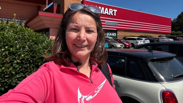A selfie of a smiling woman on a sunny day in a parking lot.
