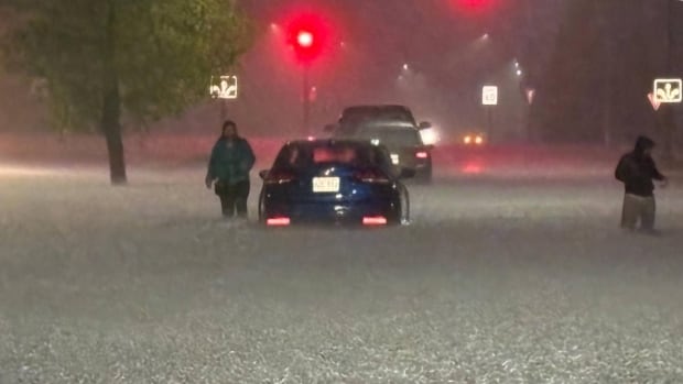 People walk stranded cars at the flooded street in a heavy downpour.