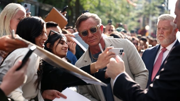 a man in a grey suit and sunglasses takes photos with fans that surround him