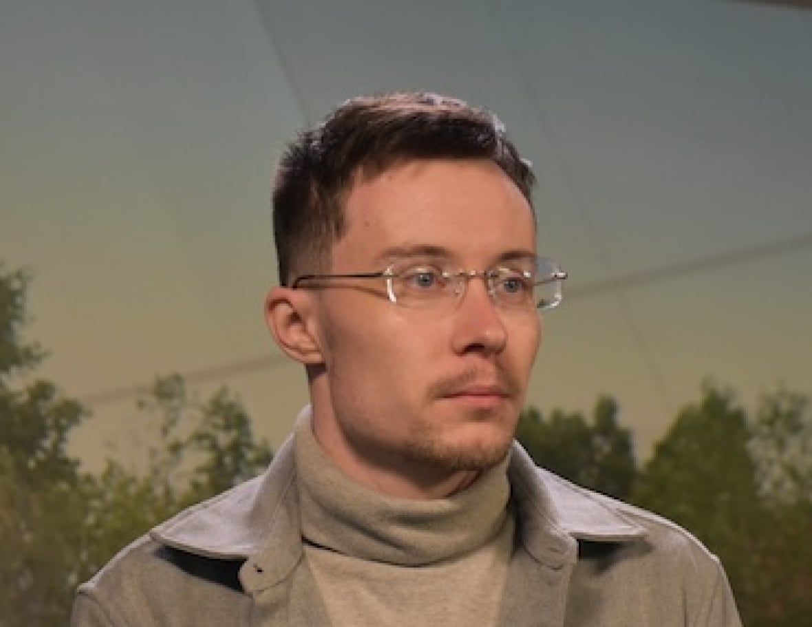 A person looks off to their left with trees and a building in the background. 