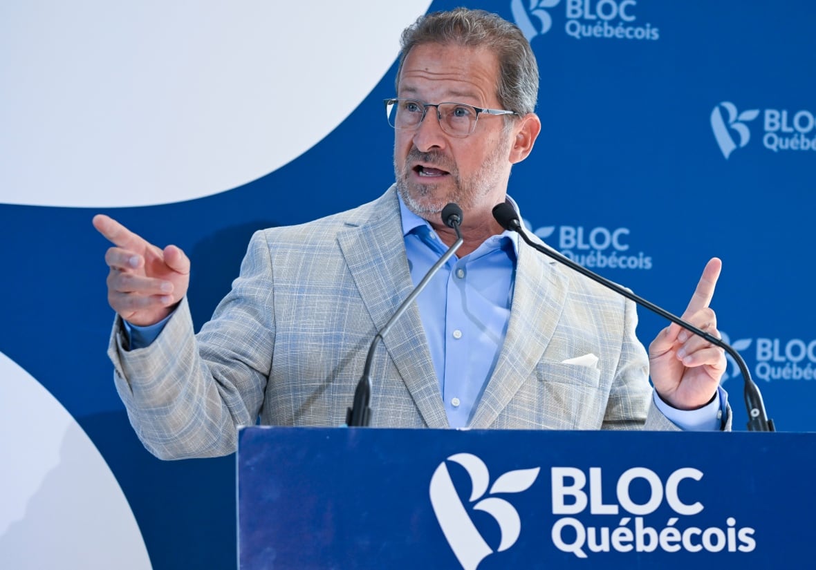 A man gestures with his hands as he speaks at a podium.