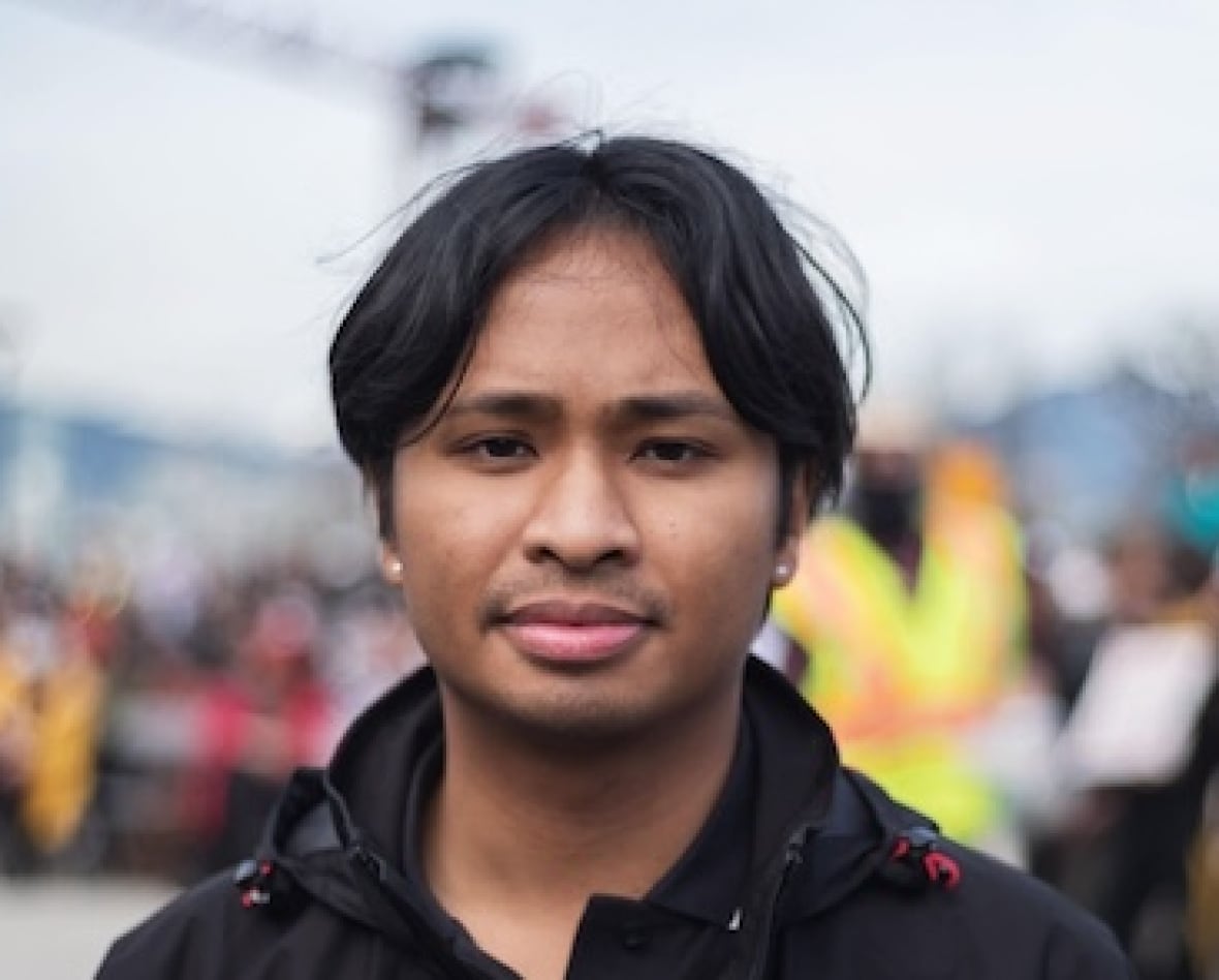 A person stands with a crowd in the background.