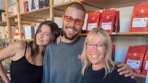 Three people smile and pose for a photo in front of bagged coffee on shelves