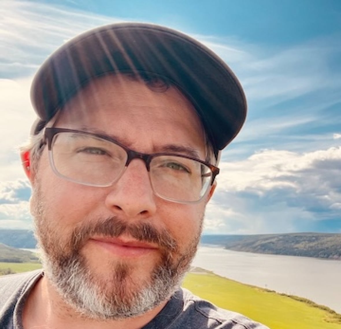 A person takes a selfie with a wide river in the background.