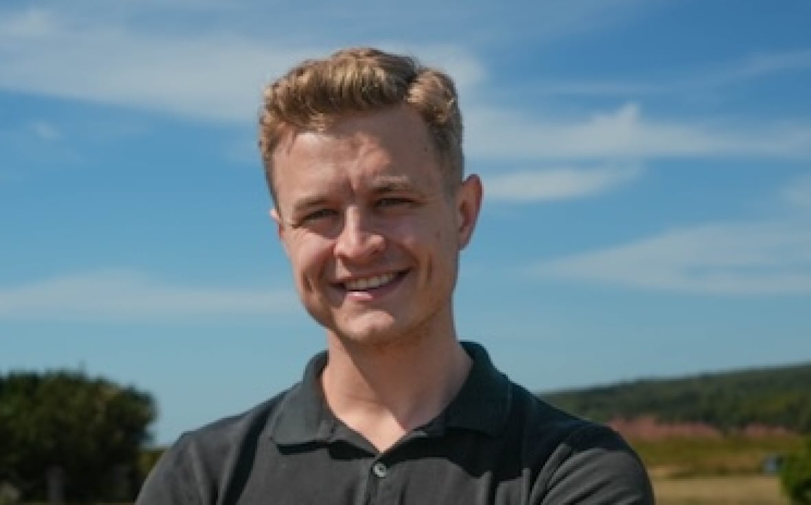 A person stands with their hands crossed with a lighthouse in the background.