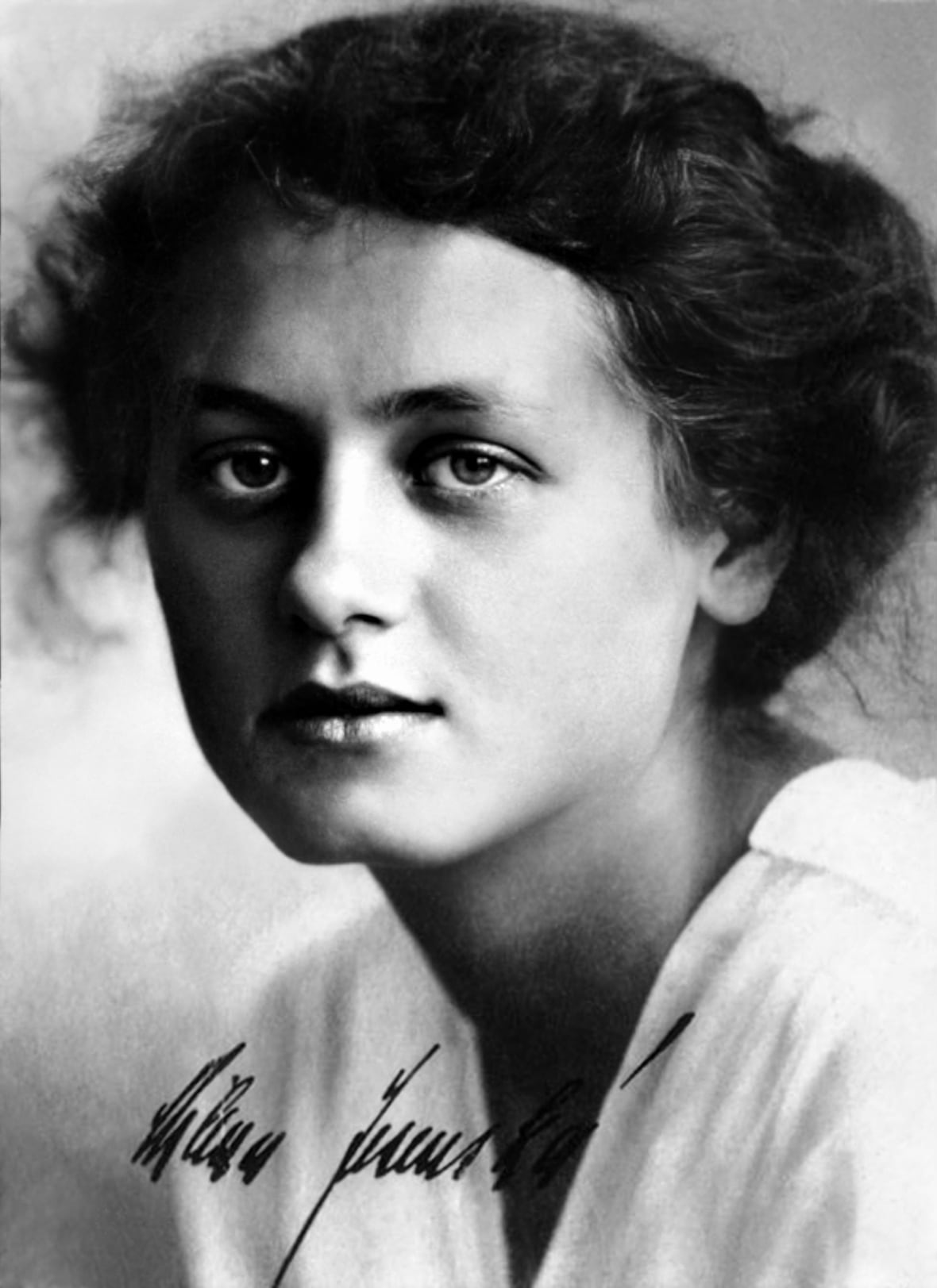 A black and white image of a woman with curly brown hair tied. 