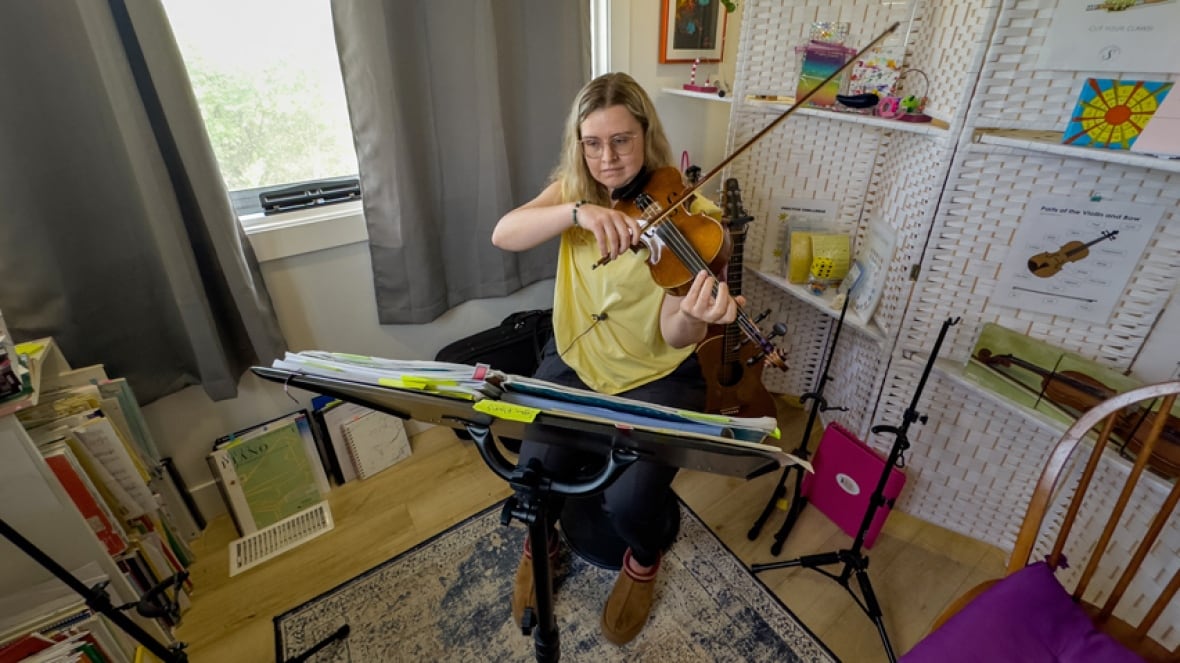 A woman sitting in a living room in front of music sheets on a stand, playing a violin.