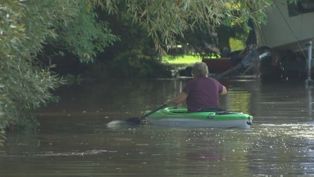 A woman is seen from the rear, paddling away in a kayak down a flooded street.