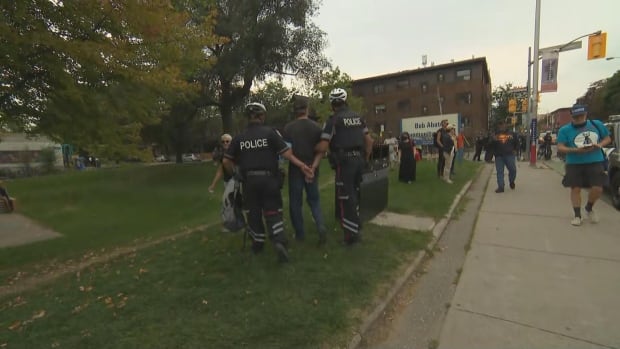 Man in handcuffs and hands behind his back being escorted by two cops in a park