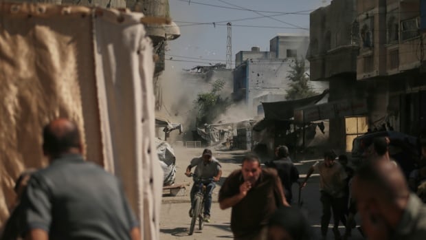 People run for cover after a rocket strikes buildings in a city.