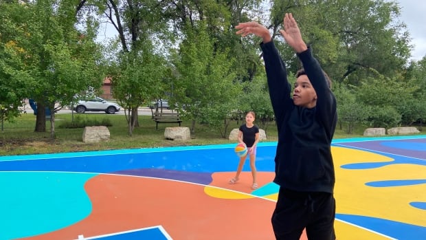A boy in a black shirt and pants shoots a basketball, 