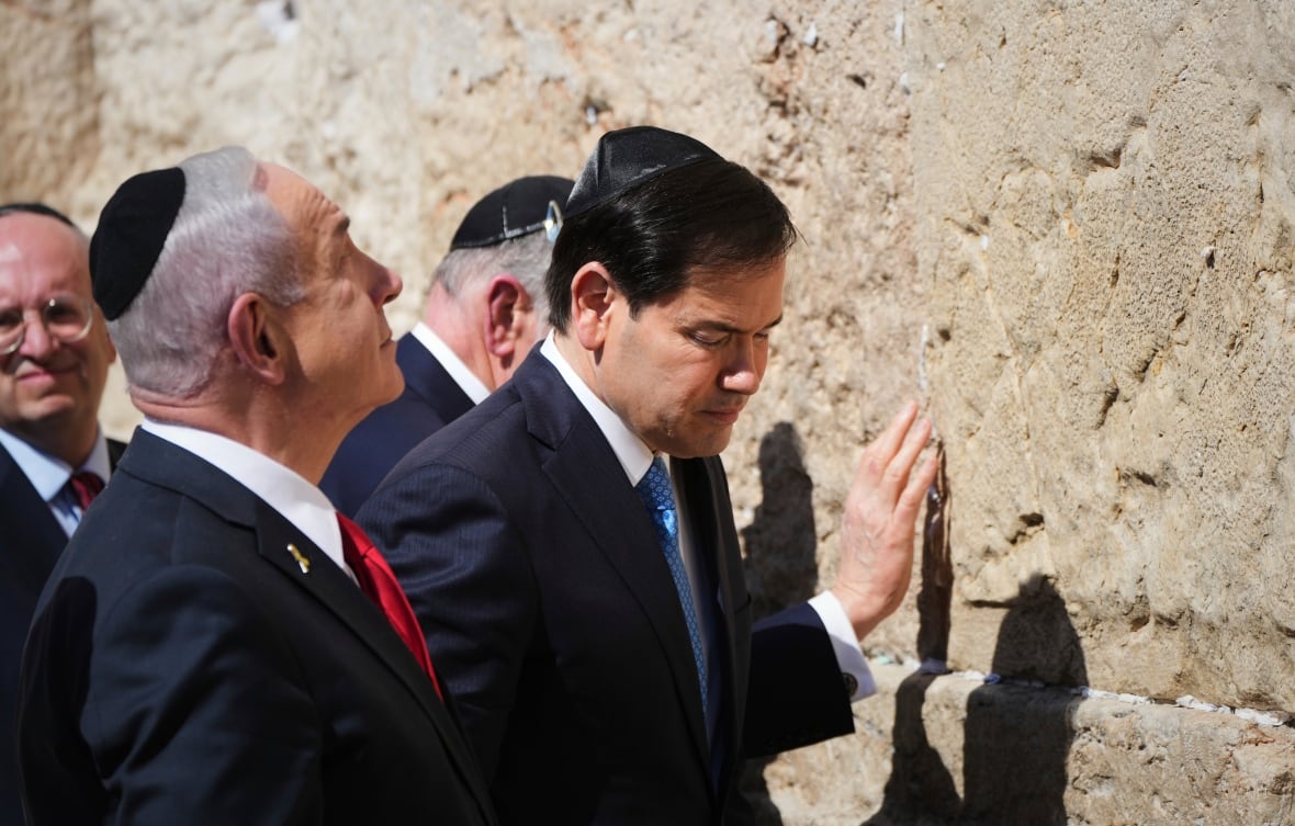 Men in suits touch a stone wall.