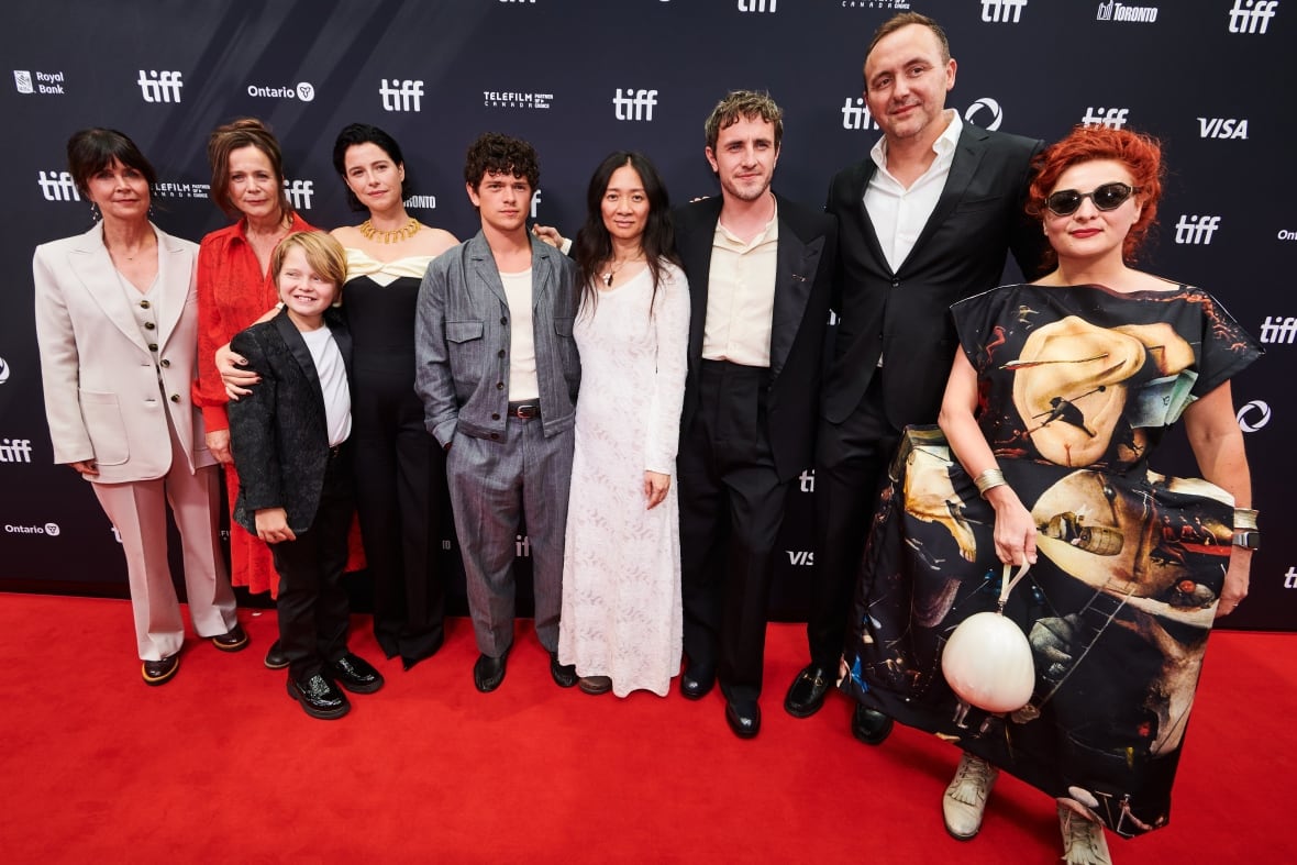 Nine people pose together on a red carpet. 