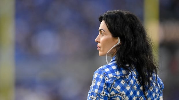 A woman in a  checkered shirt wearing a headset looks out over a football field