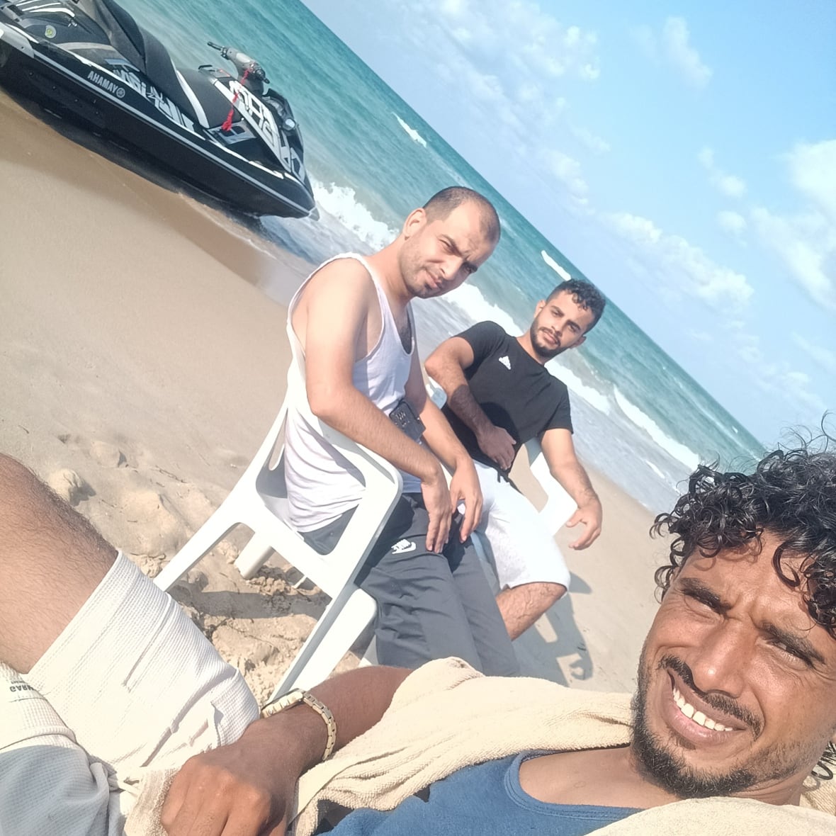 Three men sit on chairs along the Gaza coast.