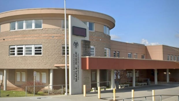 A brown brick public building with a prominent round section on a sunny dat. There's a vertical sign with Maple Ridge Secondary in English and French