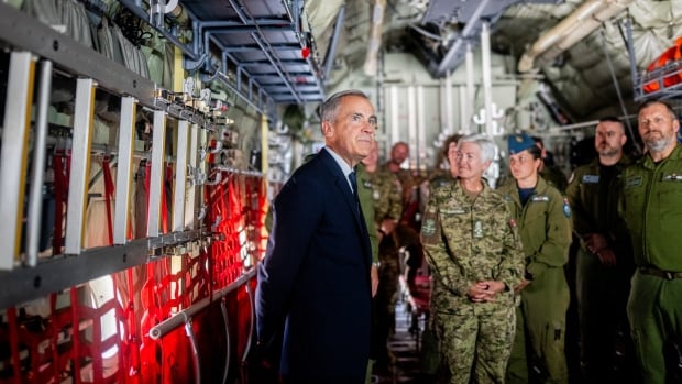 A man examines a military aircraft fuselage with military members around him.